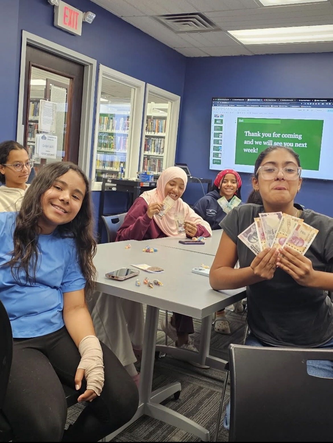 Students smiling and holding up play money during a Penny Power Project session at Roseland Free Public Library